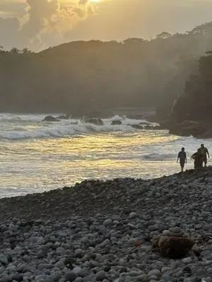 two people walking on a rocky beach near the ocean at La ceibasurf in La Libertad