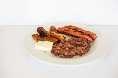 a plate of food with sausage and bacon at Hostal Casa del Sol in Suchitoto