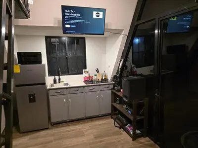a kitchen with a sink and a refrigerator and a tv at Cozy A-Frame Beach Cabin Sihu-A Casa in Las Piedras