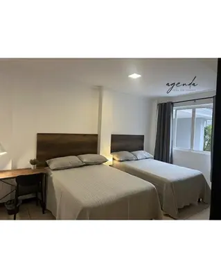 a bedroom with two beds and a desk and a window at Agenda Hotel in San Salvador
