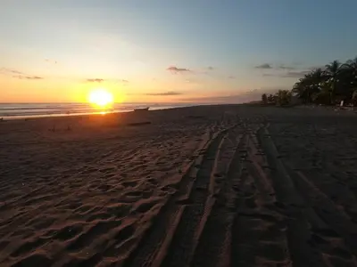 a sunset on a beach with footprints in the sand at BuenaMar Malibu Beach in Sonsonate
