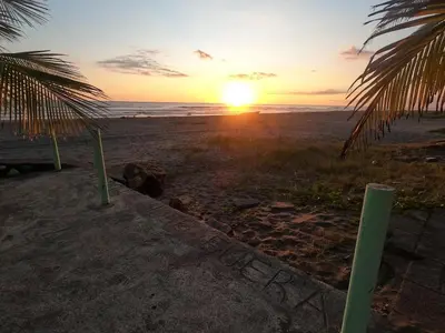 a sunset on a beach with palm trees and the ocean at BuenaMar Malibu Beach in Sonsonate