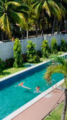 two people swimming in a swimming pool with palm trees at Sunsets Apartment in San Luis La Herradura