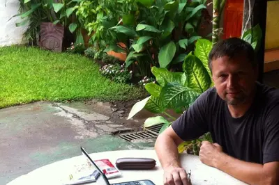 a man sitting at a table next to a surfboard at Hotel Caleta in San Miguel