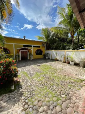 a yellow house with palm trees and a stone driveway at Casa de Playa en Atami, La Libertad, El Salvador in El Zonte