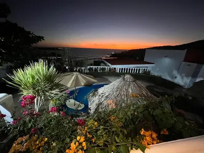 a view of a pool with an umbrella and flowers at Mar y Cielo Beach House in Tamanique