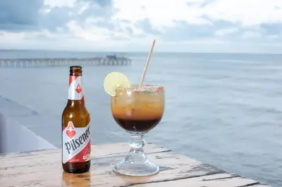 a drink and a bottle of beer on a table near the ocean at AST Surf Hotel in La Libertad
