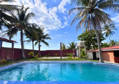 a swimming pool with palm trees in front of a house at Quinta Hojas de Mar - Frente al Mar en Playa Las Hojas in El Rosario