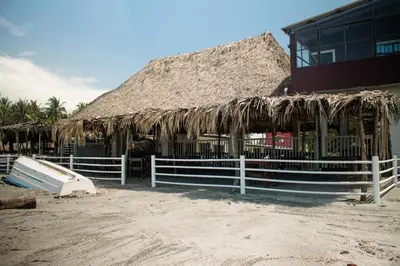a building with a straw roof and a fence at Beachfront Hotel near International Airport in Las Hojas