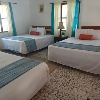 three beds in a room with blue curtains at Jardín Escondido in La Libertad