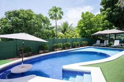 a swimming pool with an umbrella and some chairs and tables at Cala los Mangos in Tamanique