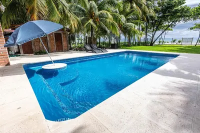 a swimming pool with an umbrella next to a house at Rancho San Jose - Barra De Santiago in Barra de Santiago