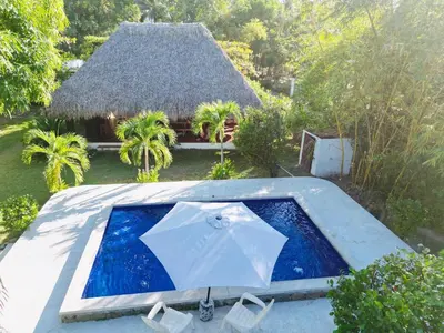 a swimming pool with an umbrella and a house at Rancho las Arantzas in Jujutla