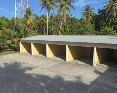 a yellow building with a white roof and palm trees at Habitacion Costabay in El Zapote