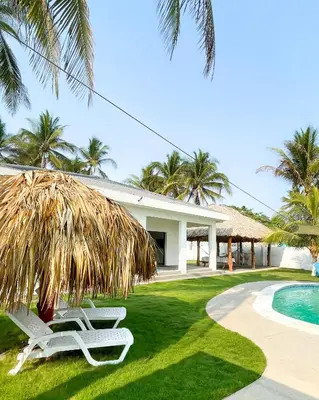 two lounge chairs under a palm tree next to a swimming pool at Azul Beach House in La Esmeralda