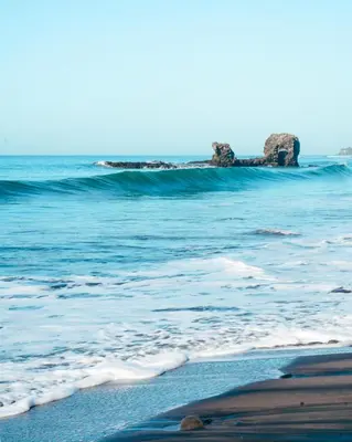 a beach with waves and rocks in the ocean at Papaya Lodge in La Libertad
