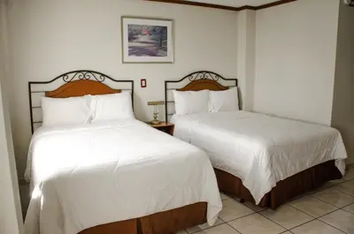 two beds in a hotel room with white sheets at Hotel Gardenia Inn in San Salvador