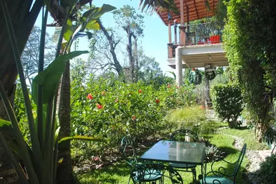 a table and chairs in a garden with a balcony at Apart Hotel Valle Verde PLANES DE RENDEROS in San Salvador