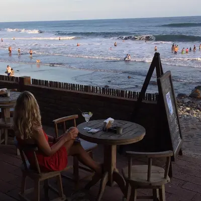 a woman sitting at a table next to the beach at Hotel & Bar La Guitarra in El Sunzal