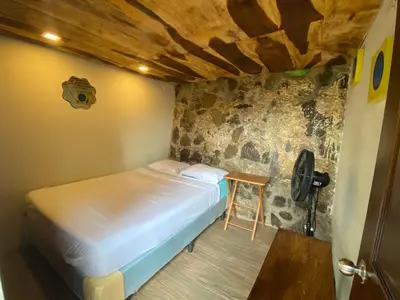 a bed in a room with a stone wall at Captain Morgan Hostel Lake Coatepeque in Santa Ana