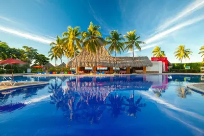 a large swimming pool with palm trees and a thatched building at Royal Decameron Salinitas - All Inclusive in Los Cóbanos
