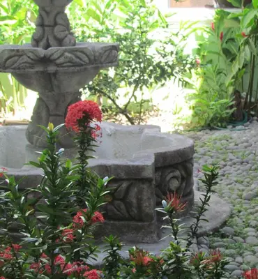 a stone fountain in a garden with a red flower at Hotel Villa Serena Escalon in San Salvador