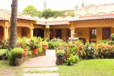 a garden in front of a yellow house with plants at Hotel Mediterraneo Plaza in San Salvador