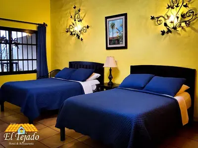 two beds in a room with yellow walls and blue sheets at El Tejado in Suchitoto
