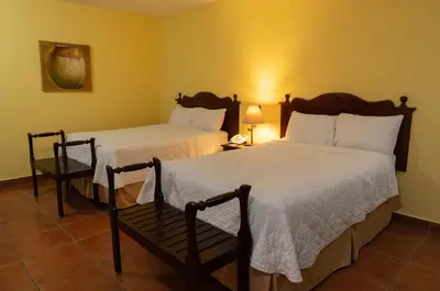 a bedroom with two beds and a chair and a lamp at Hotel Villa Terra in San Salvador