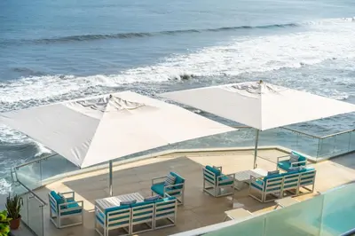 a balcony with chairs and umbrellas and the ocean at Hotel Los Farallones in La Libertad