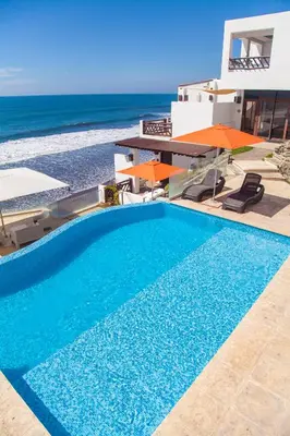 a swimming pool in front of a house with the ocean at Hotel Los Farallones in La Libertad