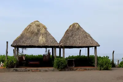 two straw umbrellas with chairs and chairs under them at Capricho Beach House in El Zapote