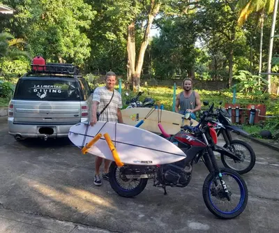 a man is standing next to a motorcycle with a surfboard at Hammock plantation in El Zonte