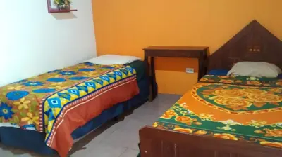 a bedroom with two beds and a table and a bed at HOSTAL CABAÑAS AVE MARIA in Concepción de Ataco