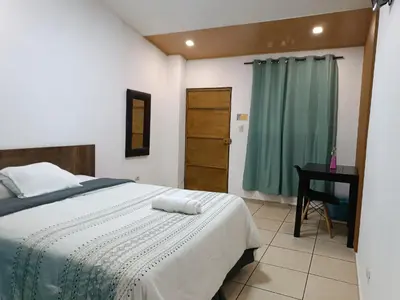 a bedroom with a bed with a desk and a green curtain at El Patio de Don Moncho in Nueva San Salvador
