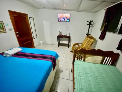 a bedroom with a bed and a chair and a tv at Nanda Parbat Hostal in San Rafael Cedros