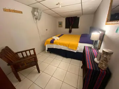 a small bedroom with a bed and a chair at Nanda Parbat Hostal in San Rafael Cedros
