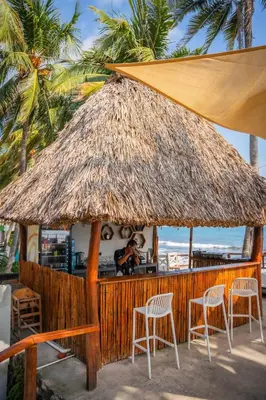 a small bar with chairs and a straw umbrella at REEF ON THE WATER in Tamanique