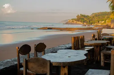 a table and chairs on a beach with the ocean at Olas Permanentes El Zonte in El Zonte