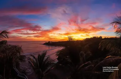 a sunset over a beach with palm trees and the ocean at Hotel Miraflores in El Cuco
