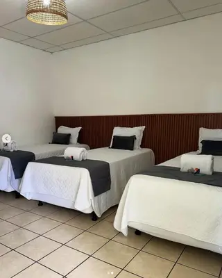 a room with three beds with white sheets at Hotel Tunco Lodge in La Libertad