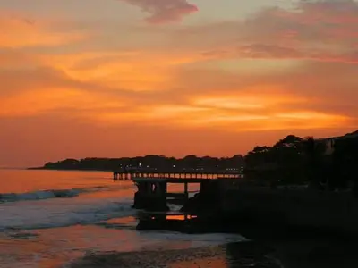 a sunset on the beach with a pier in the water at Playa El Obispo A La Marea building La Libertad in La Libertad