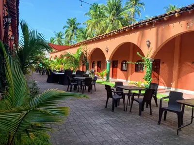 an outdoor patio with tables and chairs and palm trees at Sambo Mambo Beach Hotel in El Cuco