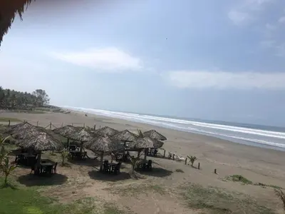 a beach with tables and straw umbrellas and the ocean at Sambo Mambo Beach Hotel in El Cuco