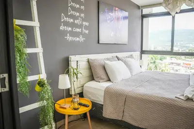 a bedroom with a bed and a table and a window at Avitat Joy 2Brm Amazing City&Volcano View Pool&Gym in San Salvador