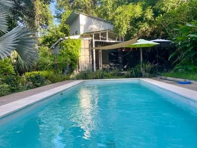 a swimming pool in front of a house with an umbrella at Wabi Sabi , casa de playa in Tamanique