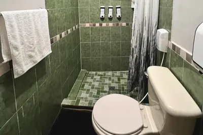 a bathroom with a white toilet in a green tiled bathroom at Quinta Sunrise, Lago de Coatepeque in El Congo