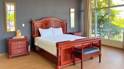 a bedroom with a wooden bed with a chair and a window at Quinta Sunset, Lago de Coatepeque in El Congo