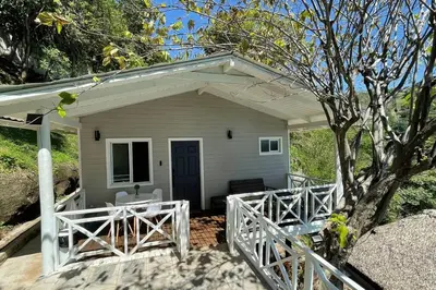 a white house with a porch and a tree at Treehouse in Tamanique