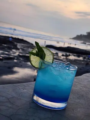 a blue drink with a lime on a table near the ocean at LOOKING2GOOD in El Zonte